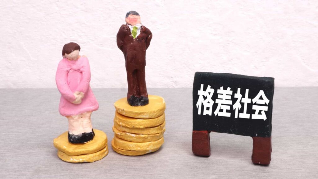 格差社会のイメージ画像。多くのお金の上に乗った男性と、少ないお金の上に乗った女性が粘土で作られている。その横に格差社会と書かれた、粘土で作った黒板がおかれている。