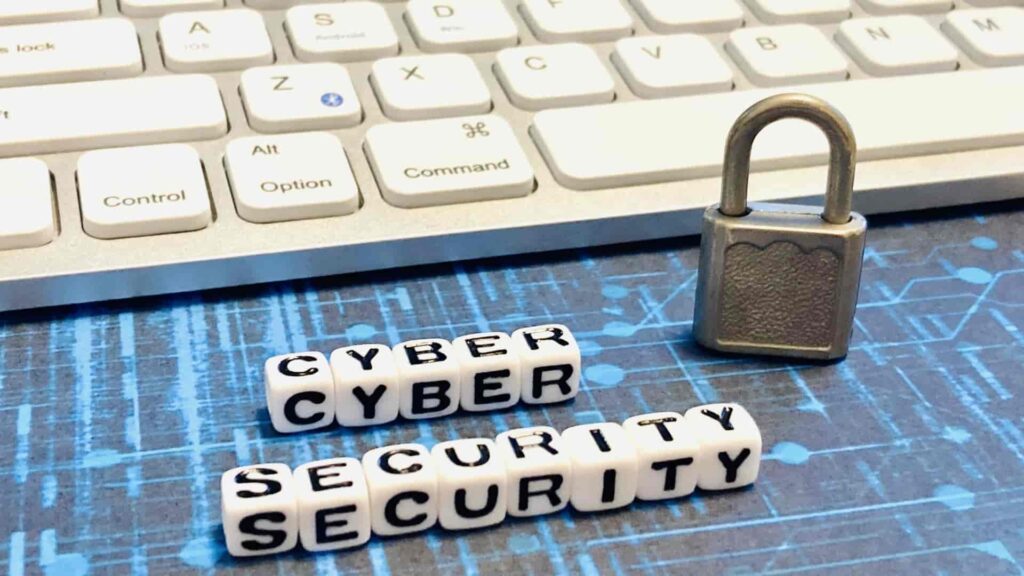 情報セキュリティのイメージ画像。ノートパソコンと鍵のかかった南京錠の横に、CYBER SECURITYと書かれたサイコロ状の置物が置かれている。